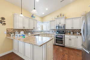 Kitchen featuring hanging light fixtures, a sink, decorative backsplash, stainless steel appliances, and a peninsula