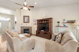 Living area featuring high vaulted ceiling, a ceiling fan, a stone fireplace, wood finished floors, and recessed lighting