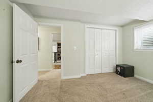 Unfurnished bedroom with a textured ceiling, baseboards, a closet, and light colored carpet
