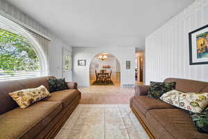 Living room featuring arched walkways, wallpapered walls, wood finished floors, and a chandelier