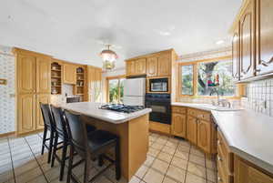 Kitchen featuring wallpapered walls, stainless steel gas cooktop, freestanding refrigerator, black oven, and a kitchen island