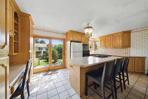 Kitchen featuring wallpapered walls, light tile patterned floors, light countertops, appliances with stainless steel finishes, and a kitchen island