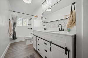 Bathroom featuring tasteful backsplash, double vanity, toilet, and a sink