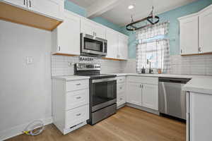 Kitchen with stainless steel appliances, light countertops, a sink, light wood-style floors, and white cabinetry