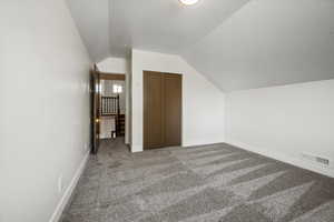 Additional living space with a textured ceiling, baseboards, lofted ceiling, carpet flooring, and visible vents
