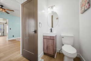Bathroom featuring wood finished floors, vanity, ceiling fan, baseboards, and toilet