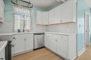 Kitchen featuring white cabinets, light wood-style flooring, tasteful backsplash, light countertops, and appliances with stainless steel finishes