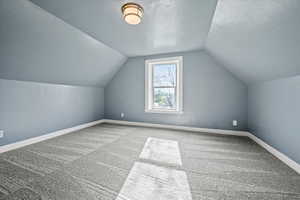 Bonus room with carpet, vaulted ceiling, a textured ceiling, and baseboards
