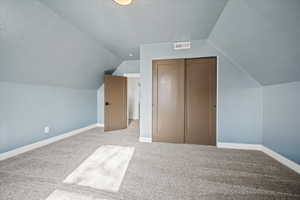 Bonus room featuring lofted ceiling, carpet flooring, visible vents, and baseboards