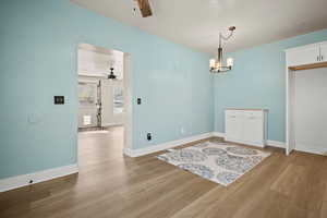 Spare room featuring wood finished floors, baseboards, and ceiling fan with notable chandelier