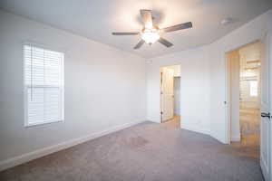 Unfurnished bedroom with a walk in closet, carpet, a ceiling fan, and baseboards