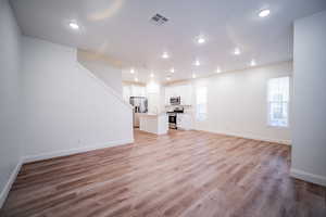 Unfurnished living room with light wood-style flooring, a sink, baseboards, visible vents, and stairway