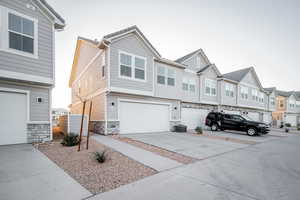 View of front facade featuring an attached garage, driveway, stone siding, and a residential view