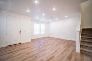 Unfurnished living room with light wood finished floors, visible vents, recessed lighting, and stairway