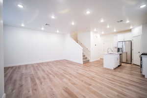 Unfurnished living room with stairway, light wood finished floors, a sink, and visible vents