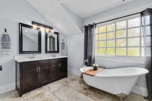 Bathroom featuring vaulted ceiling, a freestanding bath, baseboards, and a sink