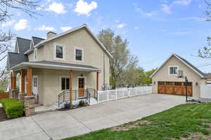 View of side of home with roof with shingles, a detached garage, a porch, fence, and stucco siding