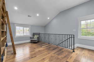 Living area with recessed lighting, hardwood / wood-style floors, vaulted ceiling, an upstairs landing, and baseboards