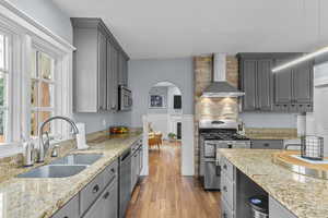 Kitchen featuring a sink, light wood-style flooring, wall chimney exhaust hood, appliances with stainless steel finishes, and gray cabinetry