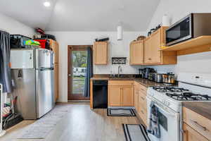 Kitchen featuring vaulted ceiling, light brown cabinetry, a sink, and appliances with stainless steel finishes