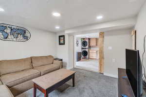 Living area featuring light colored carpet, baseboards, stacked washer / dryer, and a textured ceiling