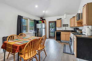 Kitchen with light wood-style flooring, light brown cabinetry, dark countertops, vaulted ceiling, and appliances with stainless steel finishes