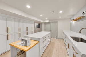 Kitchen featuring a sink, wood counters, light wood-type flooring, white cabinets, and a kitchen island