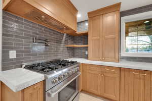 Kitchen with recessed lighting, light stone counters, open shelves, high end stainless steel range oven, and tasteful backsplash