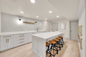 Kitchen with a sink, a breakfast bar, light wood finished floors, light countertops, and a kitchen island