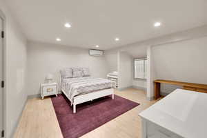 Bedroom with recessed lighting, a wall mounted air conditioner, baseboards, and light wood-type flooring