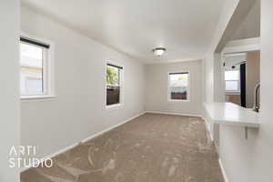 Unfurnished dining area with baseboards, carpet flooring, a sink, and a healthy amount of sunlight