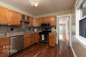 Kitchen with appliances with stainless steel finishes, tasteful backsplash, a sink, and dark wood-type flooring