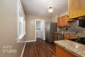 Kitchen featuring a sink, decorative backsplash, appliances with stainless steel finishes, baseboards, and washer / clothes dryer