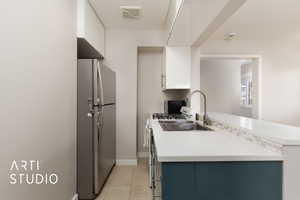 Kitchen with light tile patterned floors, light countertops, white cabinets, visible vents, and freestanding refrigerator