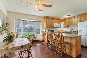Kitchen with light stone counters, a textured ceiling, white appliances, ceiling fan, and dark wood-style floors