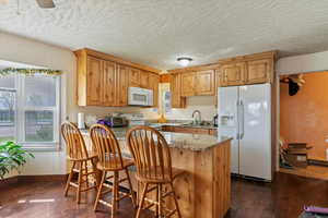 Kitchen featuring dark wood-style floors, a sink, baseboards, white appliances, and light stone counters