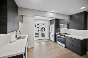 Kitchen featuring light countertops, modern cabinets, a sink, light wood-type flooring, and appliances with stainless steel finishes