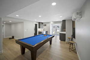 Recreation room featuring baseboards, a textured ceiling, light wood-type flooring, and a wall unit AC