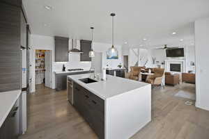 Kitchen featuring stainless steel appliances, light countertops, wall chimney range hood, a sink, and modern cabinets