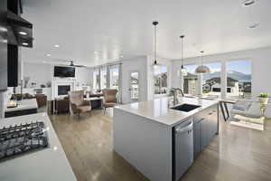 Kitchen featuring a sink, light wood-style floors, a ceiling fan, light countertops, and a fireplace