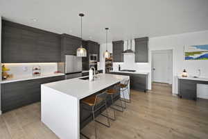 Kitchen featuring modern cabinets, wall chimney range hood, decorative backsplash, and a kitchen bar