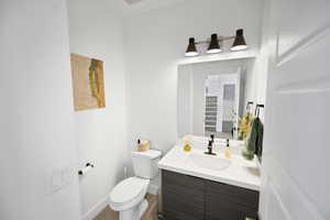 Half bath featuring wood finished floors, vanity, baseboards, toilet, and visible vents