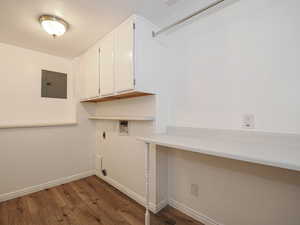 Clothes washing area with electric panel, hookup for an electric dryer, hookup for a washing machine, wood finished floors, and cabinet space
