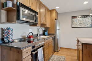Kitchen with stainless steel appliances, light wood-style flooring, a sink, dark countertops, and recessed lighting