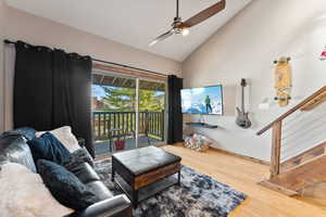 Living area with baseboards, wood finished floors, stairs, ceiling fan, and high vaulted ceiling