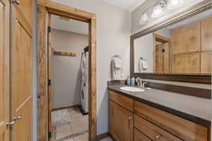 Bathroom with tile patterned flooring, baseboards, stacked washer / dryer, and vanity