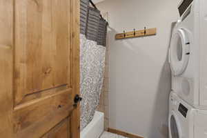 Clothes washing area with stacked washer and dryer, baseboards, and laundry area