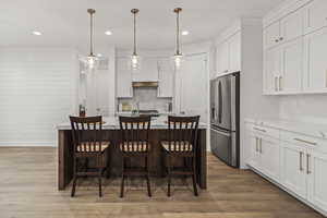 Kitchen featuring stainless steel refrigerator with ice dispenser, light countertops, white cabinetry, and tasteful backsplash