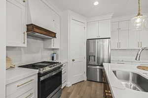 Kitchen featuring custom exhaust hood, appliances with stainless steel finishes, a sink, and white cabinetry