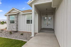 Property entrance featuring board and batten siding, stone siding, a shingled roof, and a porch